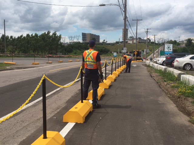 Équipe de travailleurs installant des bollards et chaînes de sécurité jaunes pour délimiter une piste cyclable